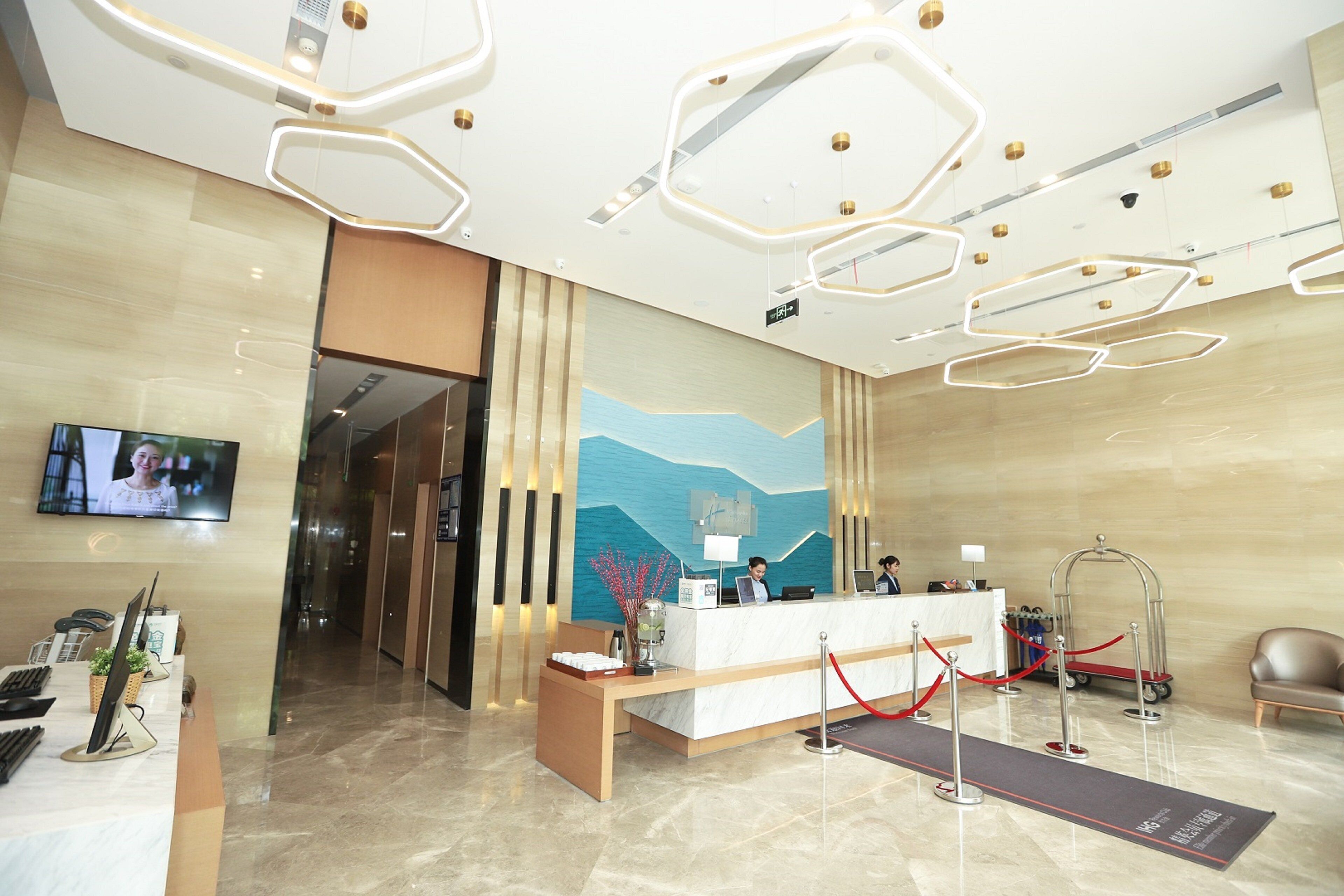 A hotel reception area with a reception desk, a TV screen, a red carpet leading to the desk, and a modern ceiling design.