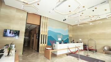 A hotel reception area with a reception desk, a TV screen, a red carpet leading to the desk, and a modern ceiling design.