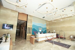 A hotel reception area with a reception desk, a TV screen, a red carpet leading to the desk, and a modern ceiling design. - Holiday Inn Express Chengdu Xindu by IHG (Chengdu)