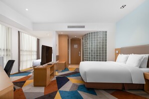 A hotel room with a bed, desk, chair, TV, and a large window with curtains.