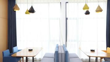 Una habitación de hotel moderna con un ventanal grande, un sofá, dos mesas y sillas azules.