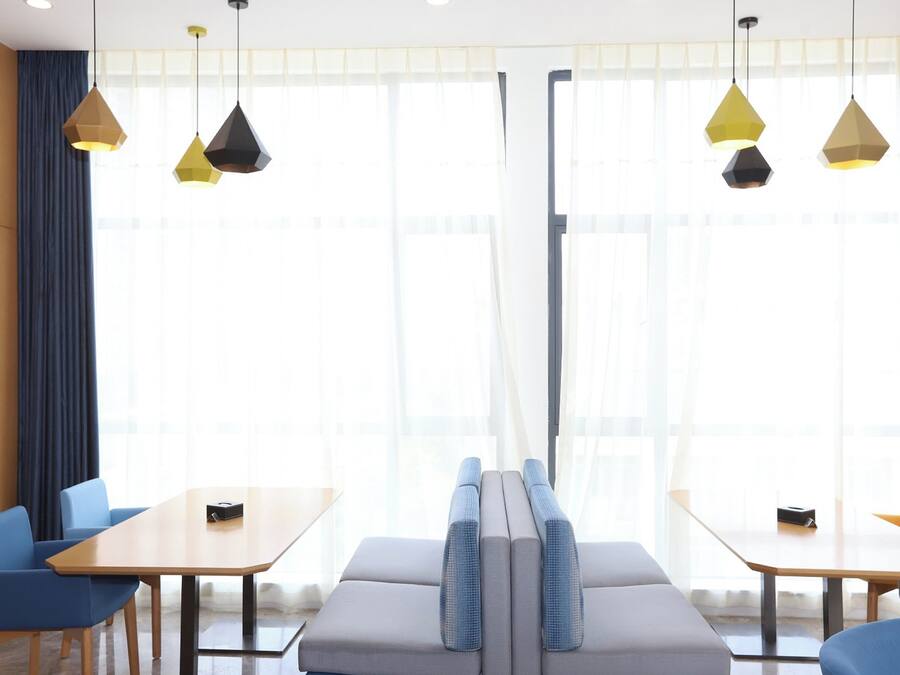 Una habitación de hotel moderna con un ventanal grande, un sofá, dos mesas y sillas azules.