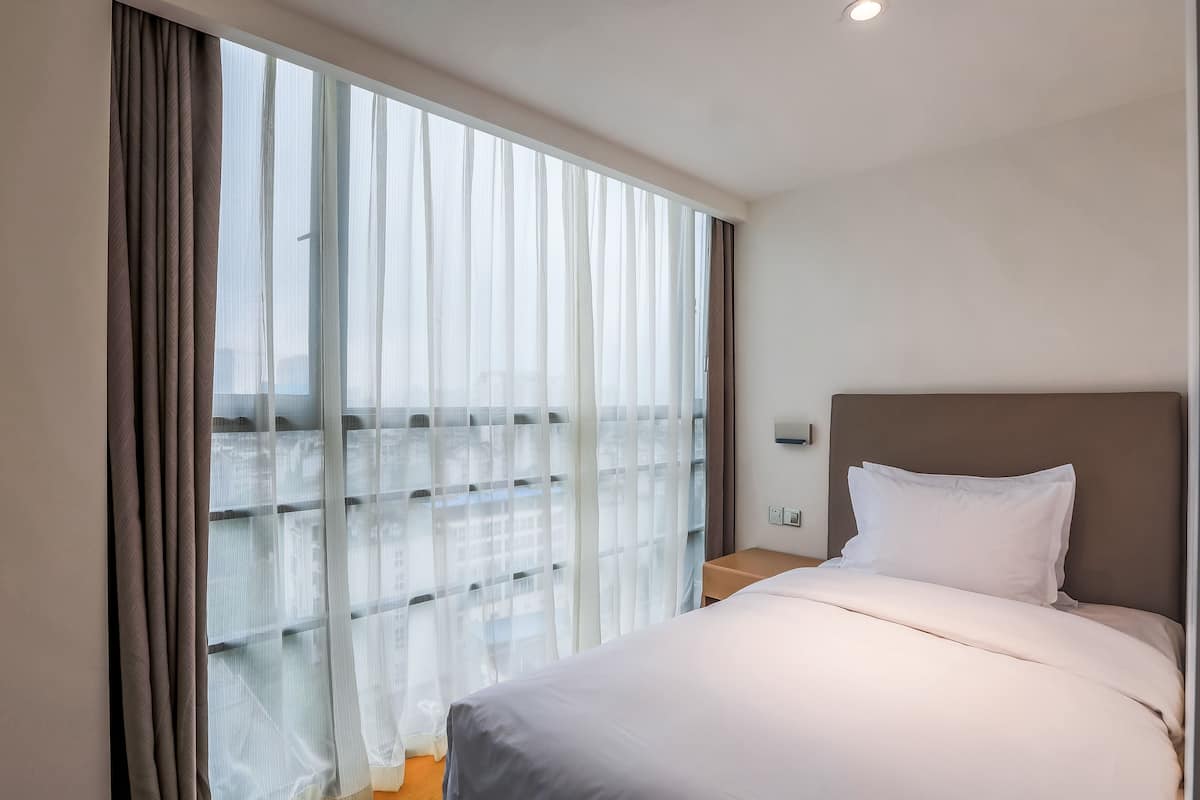A hotel room with a large window, a bed with white bedding, and a brown headboard.