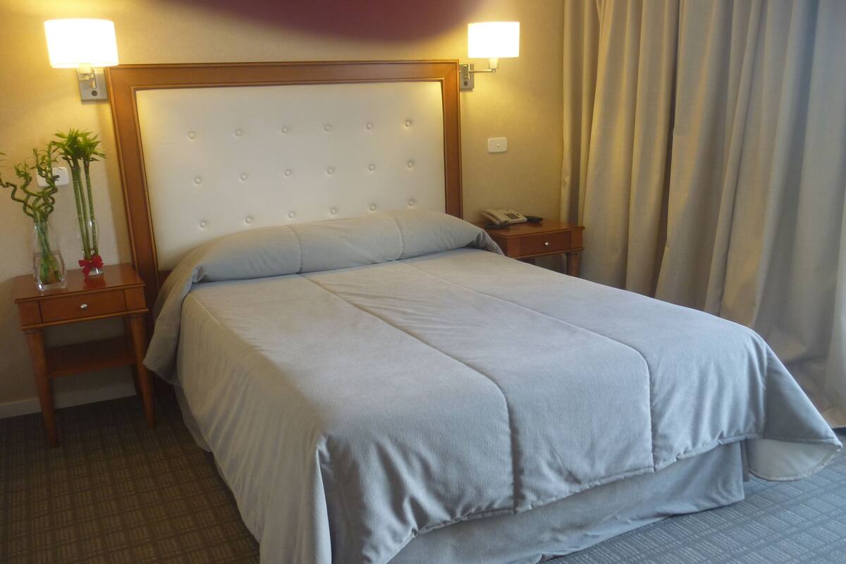 Une chambre d’hôtel avec un grand lit, deux tables de chevet, une petite table, une lampe et un téléphone.