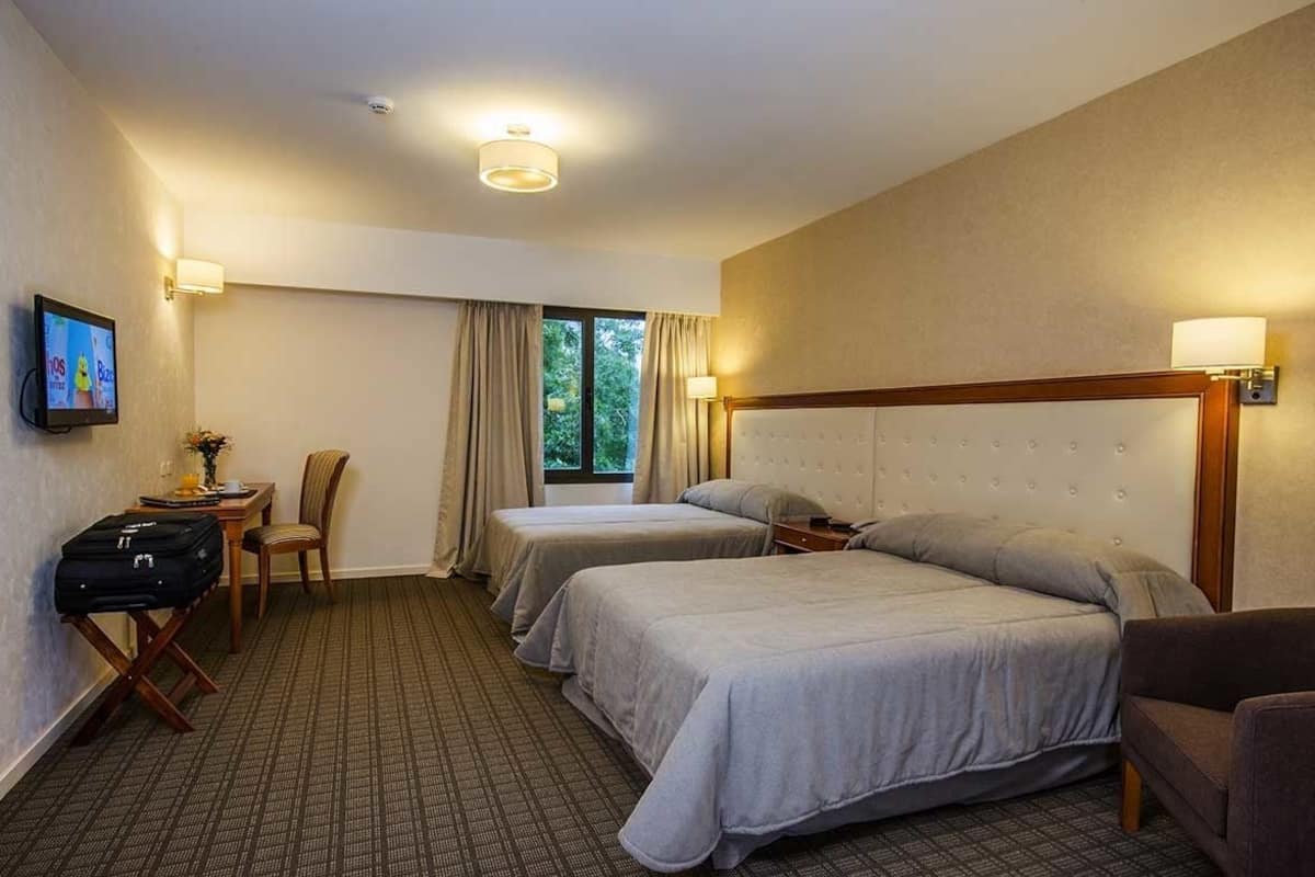Une chambre d’hôtel avec deux lits, un bureau, une chaise et un téléviseur fixé au mur.