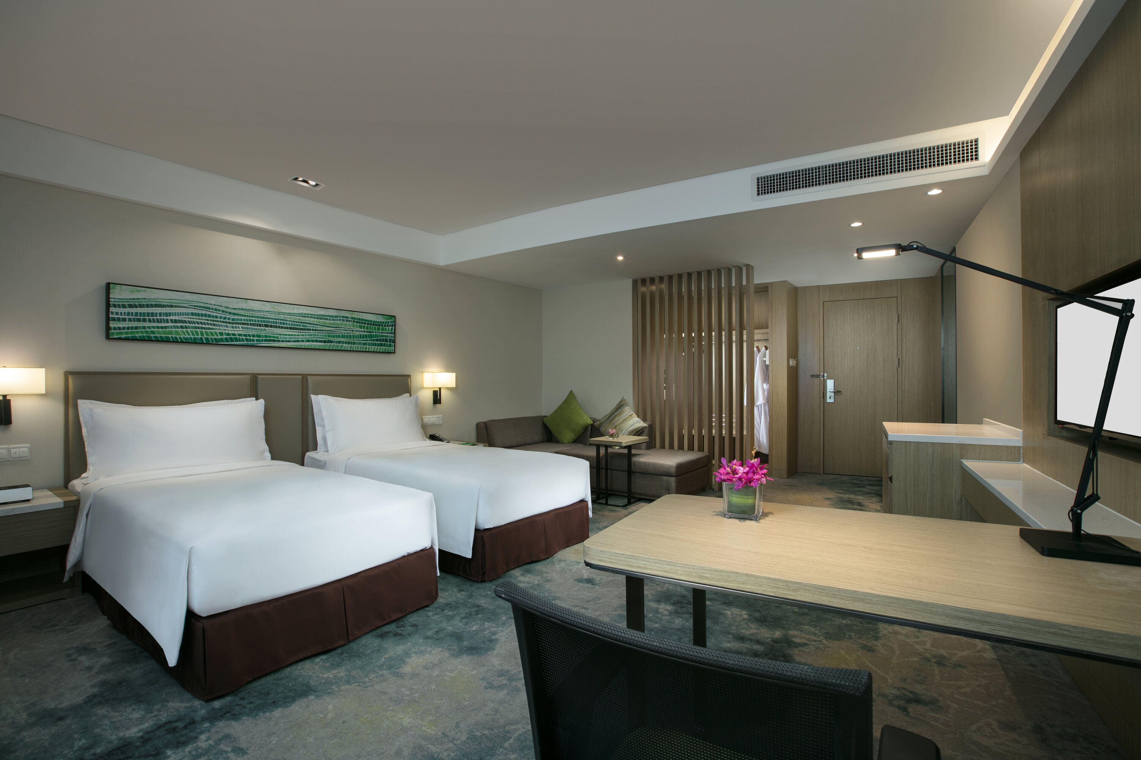 A hotel room with two beds, a desk, a chair, a lamp, and a decorative wall piece.