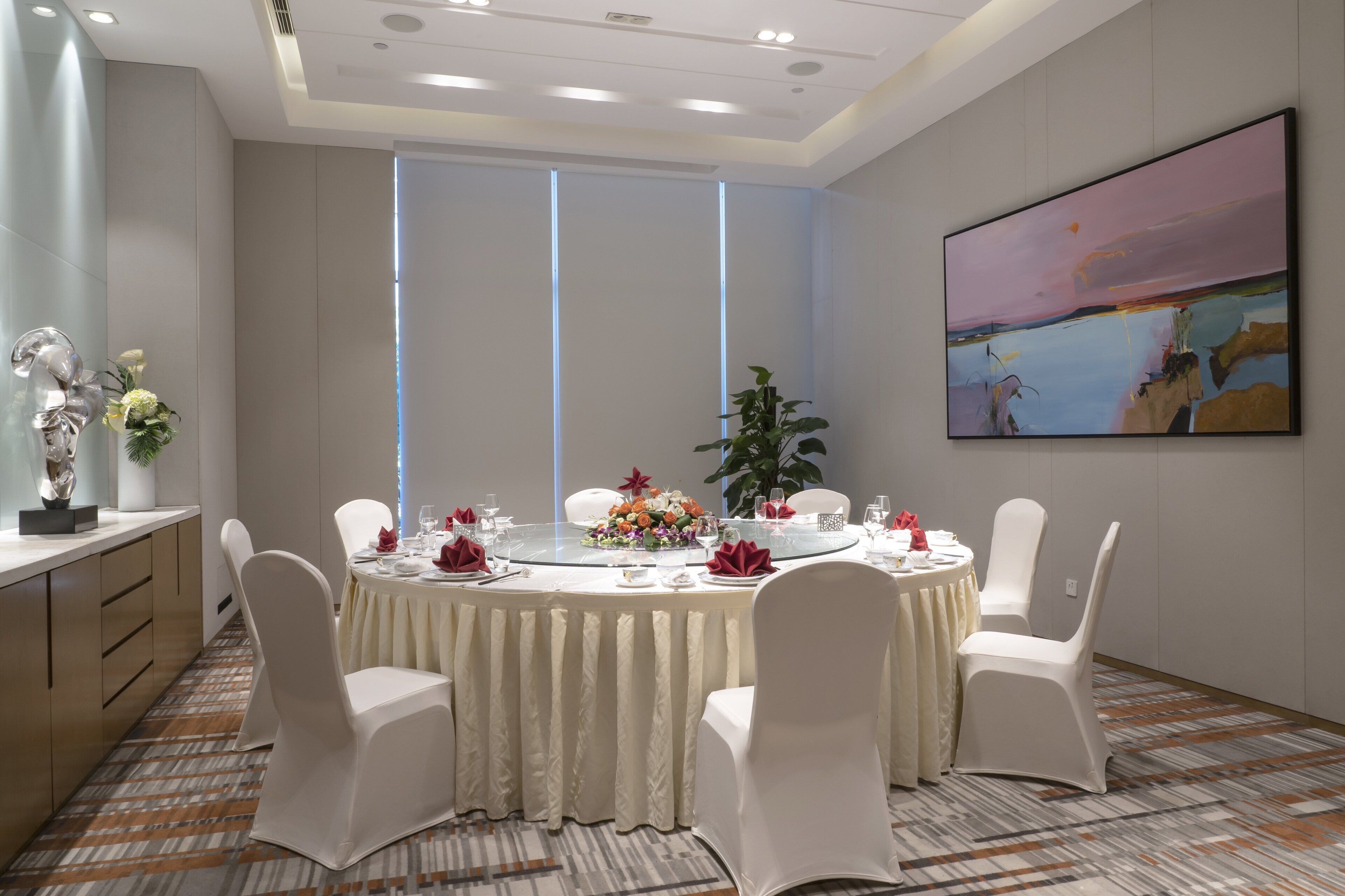 A conference room with a round table, white chairs, and a large painting on the wall.