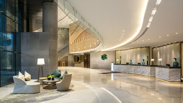 A modern hotel lobby with a curved reception desk, seating area with sofas, and a staircase leading to upper floors. - Holiday Inn Hangzhou Gongshu by IHG (Hangzhou)
