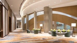 A spacious hallway with a patterned carpet, seating areas with green chairs and a sofa, and a large column. - Holiday Inn Hangzhou Gongshu by IHG (Hangzhou)