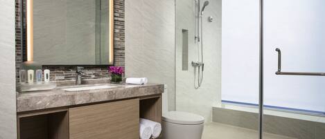 Un baño moderno con cabina de ducha de vidrio, lavamanos de mármol y muebles de madera.