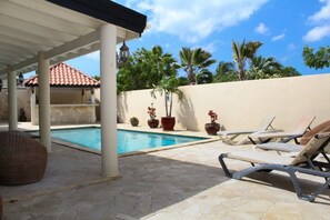A poolside area with lounge chairs, a covered patio, and potted plants. - Casa Luna (Oranjestad)