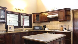 A kitchen with dark wooden cabinets, a granite countertop, a microwave, and a coffee maker. - Casa Luna (Oranjestad)