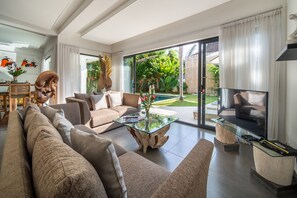 A modern living room with a glass coffee table, a sofa, and a TV on a stand. - Villa Wiana by Villa Finder (Seminyak)