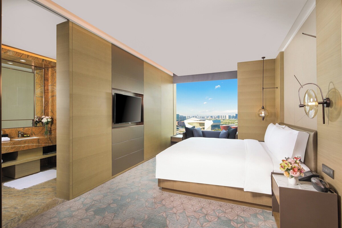 Une chambre d’hôtel avec un lit, une télévision, une salle de bain avec un miroir et une vue sur la ville.