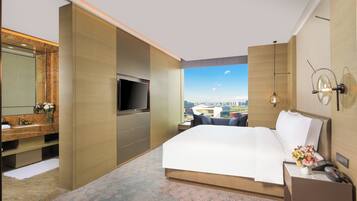 A hotel room with a bed, a TV, a bathroom with a mirror, and a city view.