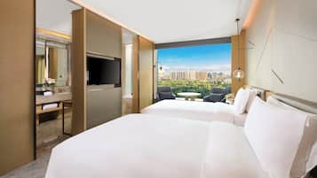 A hotel room with two beds, a desk with a TV, a bathroom, and a city view.