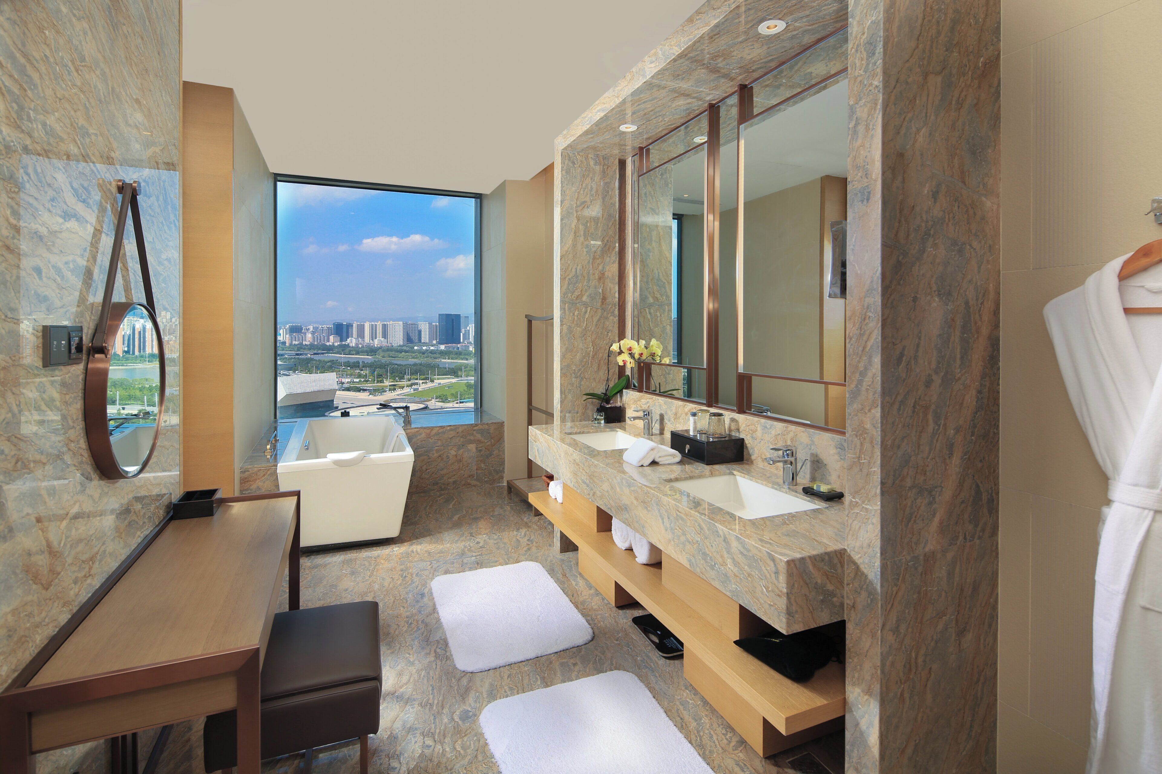 A modern bathroom with a large mirror, dual sinks, a bathtub, and a view of a cityscape.