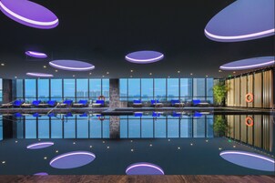 Una piscina interior moderna con sillones reclinables azules, amplias ventanas y focos circulares en el techo.