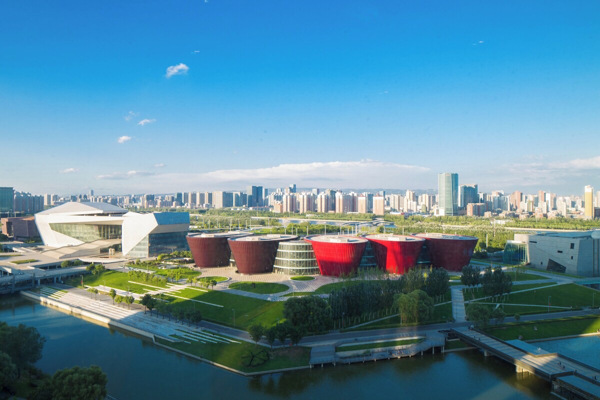 Un paysage urbain moderne avec une rivière, des bâtiments rouges aux couleurs vives et un ciel bleu dégagé.