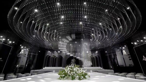 Un vaste hall doté d’un plafond élevé, illuminé de lustres étincelants, agrémenté d’un arrangement floral central et pourvu de gradins.