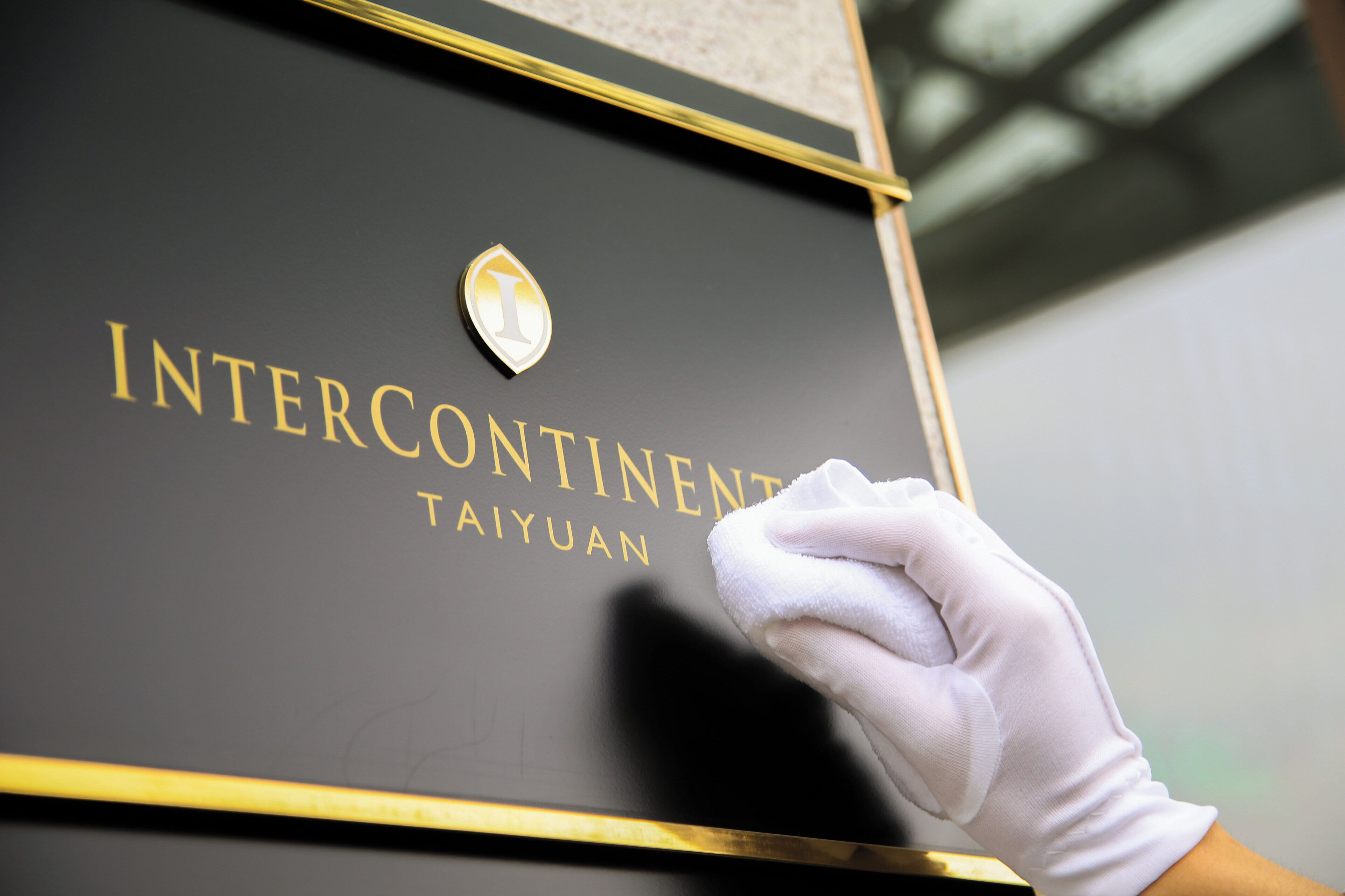 A hand wearing a glove touching a black box with gold lettering and a logo.