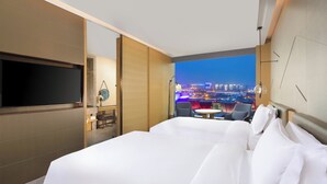 A hotel room with a large bed, a TV, a small table, and a view of a cityscape at night. - Intercontinental Taiyuan by IHG (Taiyuan)