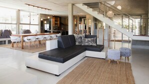 Een moderne woonkamer met een hoekbank, een eethoek met stoelen en een trap naar een hoger niveau.