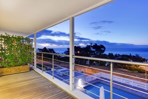 A balcony with a view of the sea, a pool, and a wooden deck.