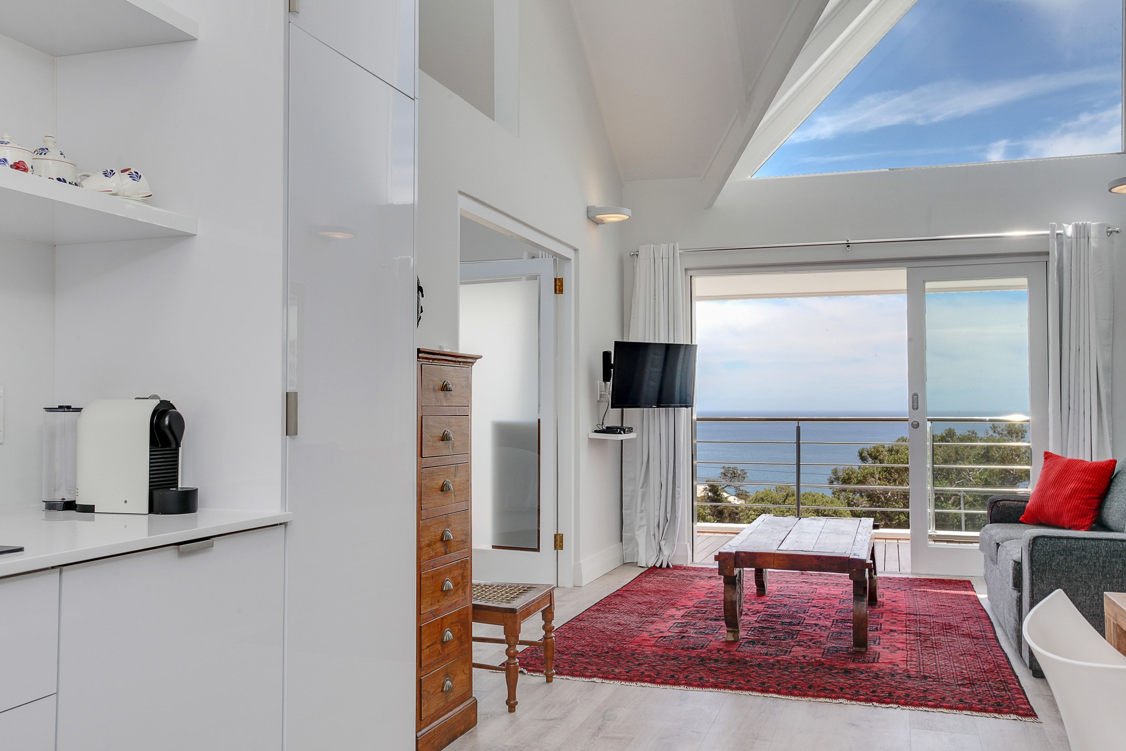 Uma sala de estar moderna com uma janela grande, uma televisão de tela plana, uma mesa de centro de madeira e um tapete vermelho.