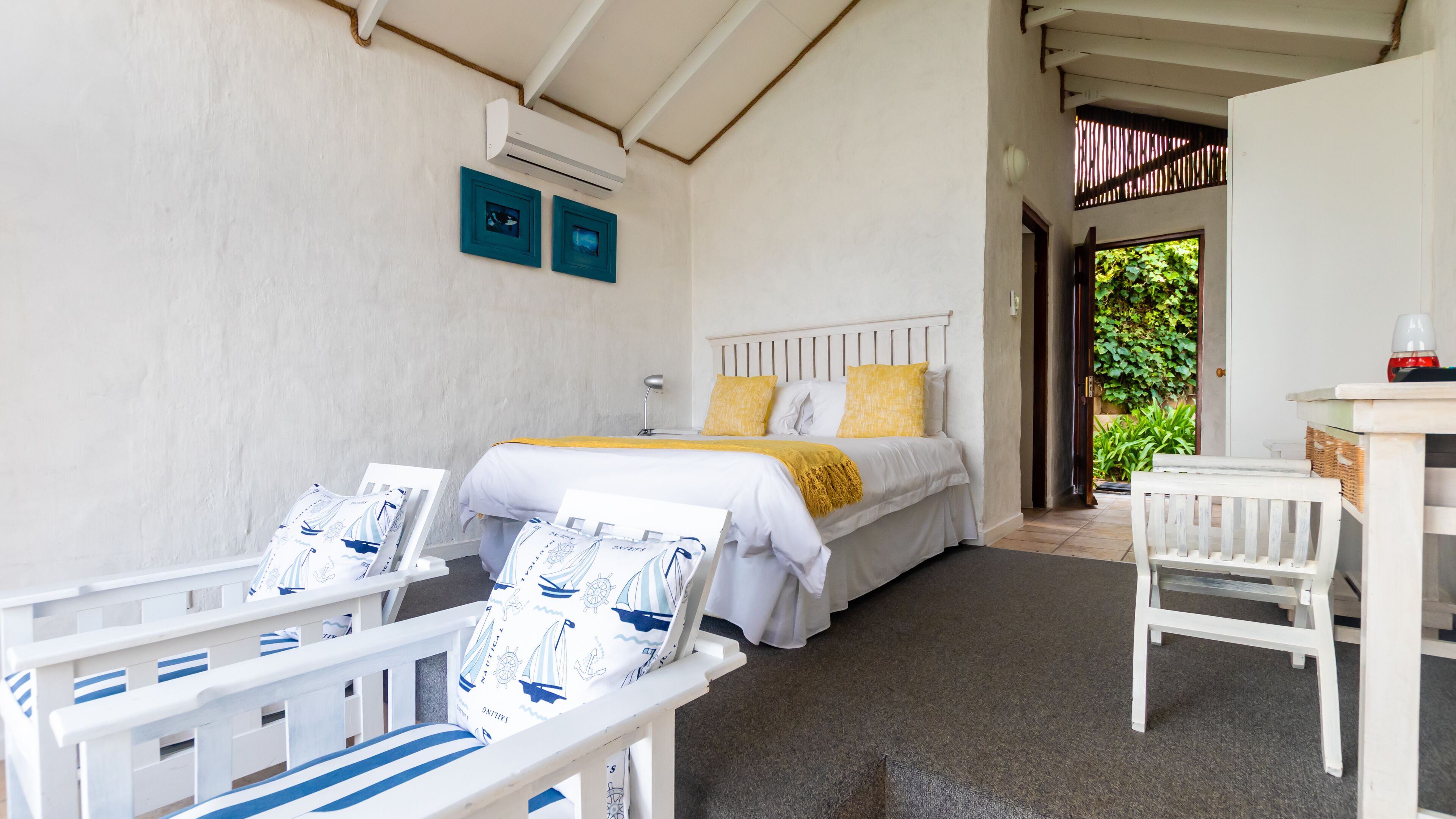 A bedroom with a bed, two chairs, a desk, and an air conditioning unit.