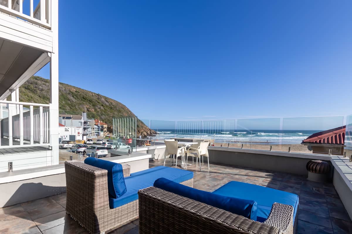 Une terrasse sur le toit, meublée de mobilier en osier, avec vue sur la plage et un ciel dégagé.