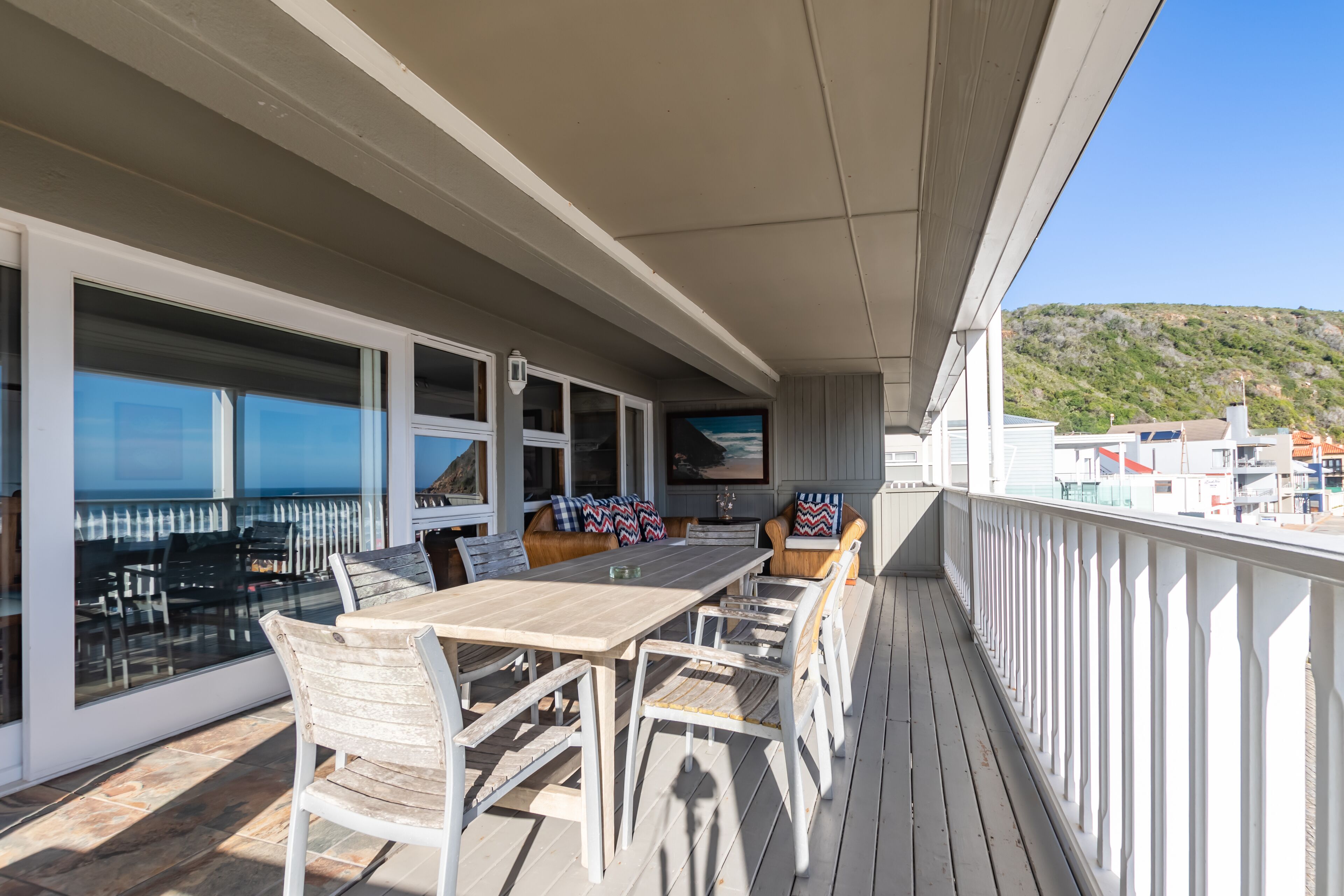 Eine überdachte Terrasse im Freien mit Essbereich, Sitzgelegenheiten und großen Fenstern.