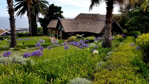 A thatched-roof building surrounded by lush gardens and palm trees.