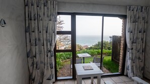A balcony with a table and chairs, a view of the sea, and a garden area.