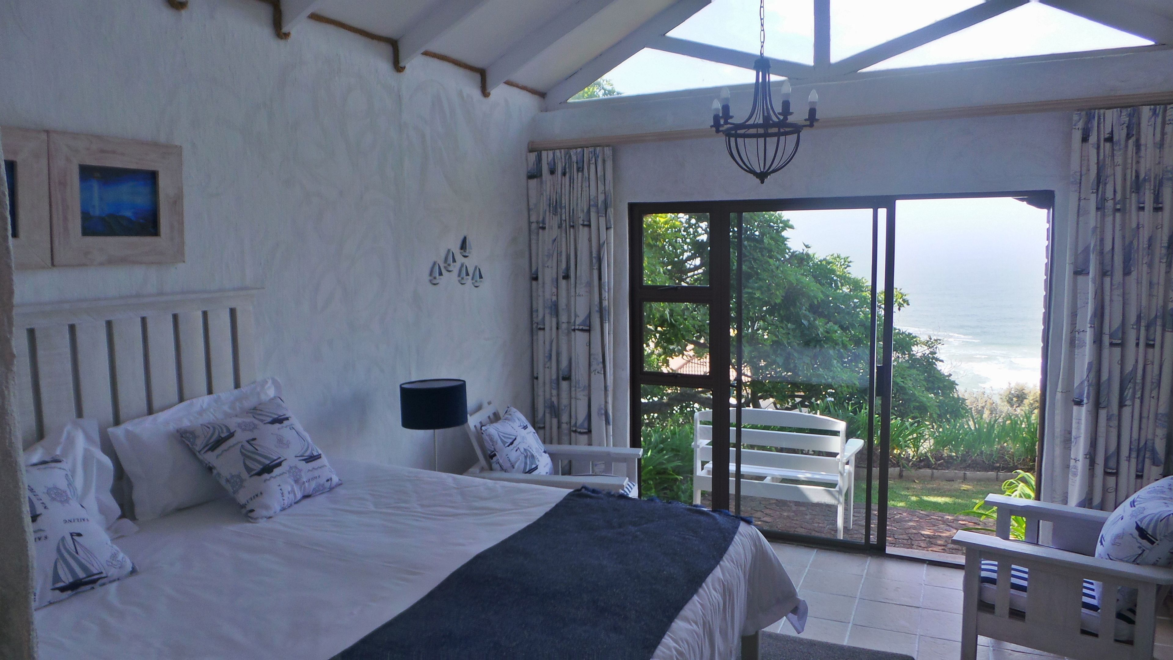 A bedroom with a bed, a nightstand, a lamp, and a view of the ocean through large sliding doors.