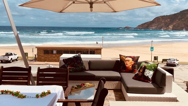 A beachside seating area with a table, chairs, and an umbrella overlooking the ocean.