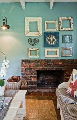 Uma sala de estar acolhedora com lareira de tijolos, parede azul e diversos quadros e relógios.
