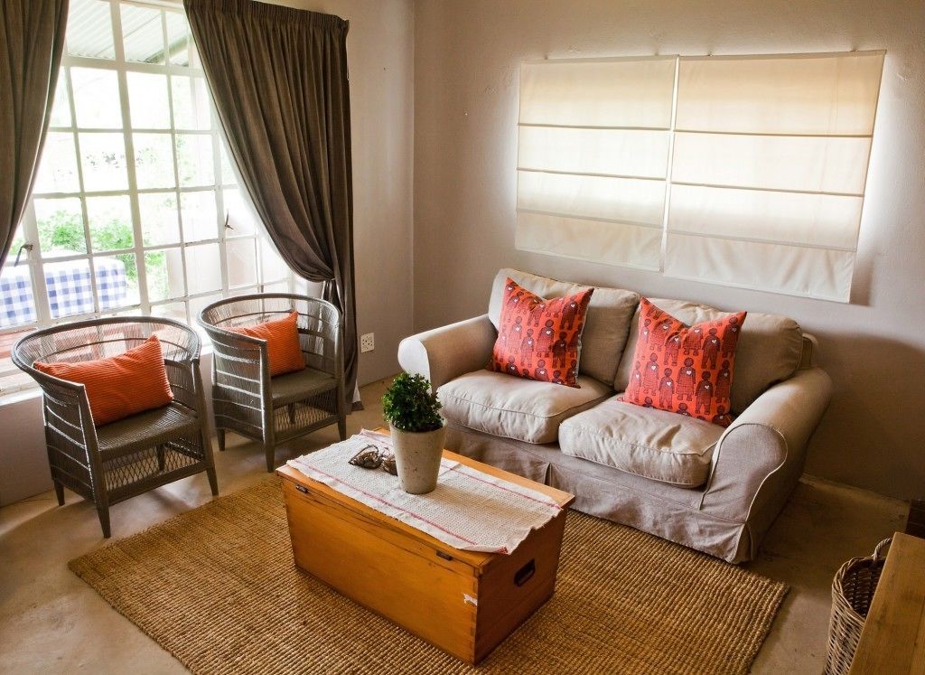 Un salón con un sofá, dos sillones, una mesa de centro de madera y una ventana con cortinas.