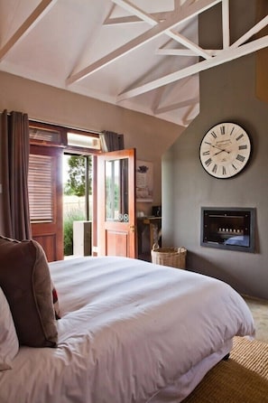 Quarto com uma cama grande, uma porta de madeira que dá para uma área externa, um relógio de parede e uma lareira.
