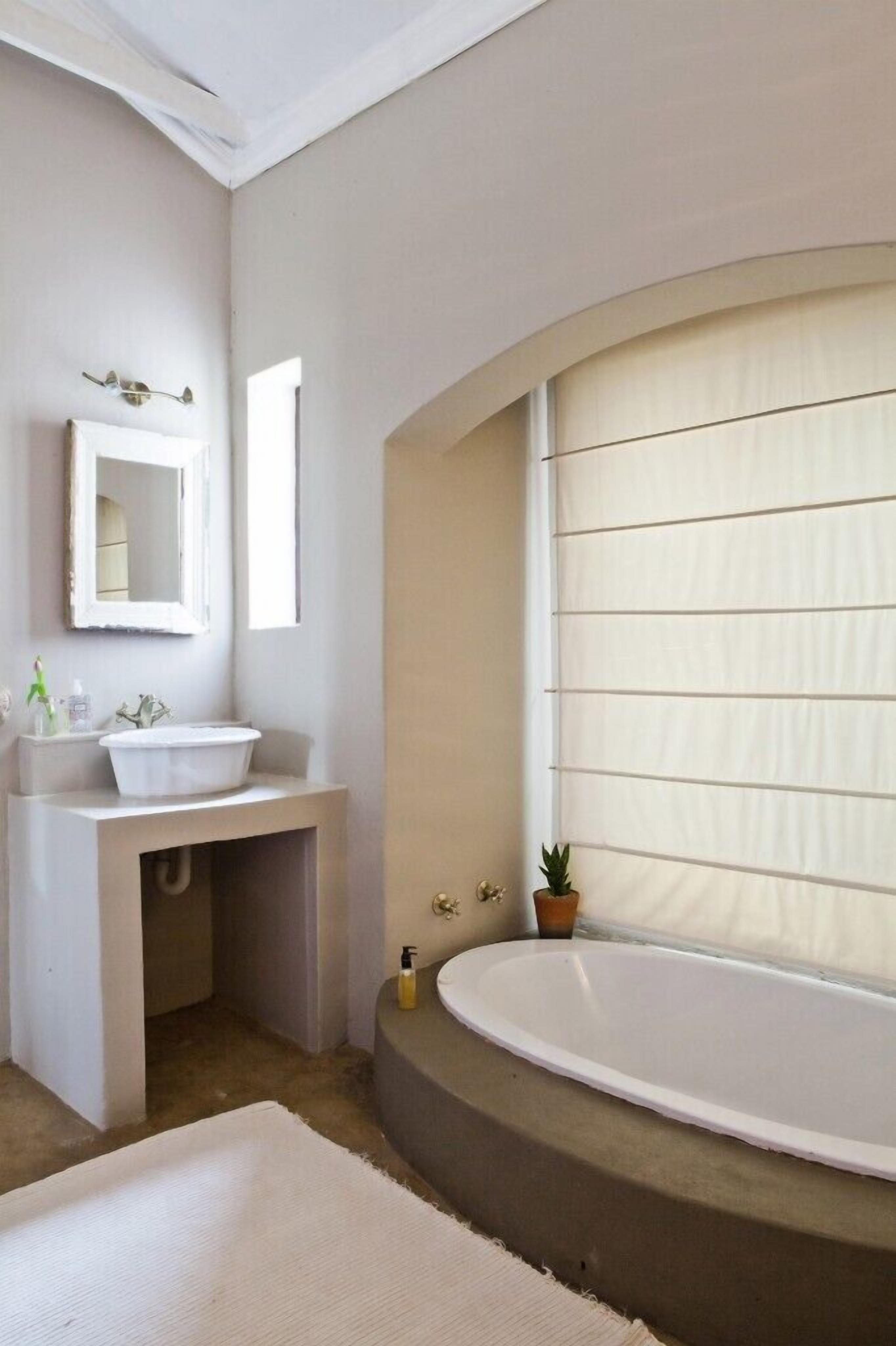 Un baño con bañera, lavamanos, espejo y ventana con persianas.