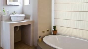 Un baño con bañera, lavamanos, espejo y ventana con persianas.