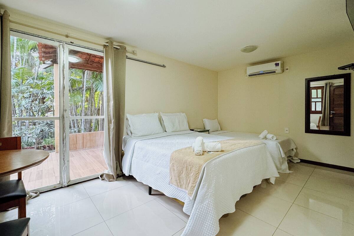 Ett hotellrum med en säng, ett litet bord, en stol, ett fönster med gardiner och en luftkonditioneringsanläggning.