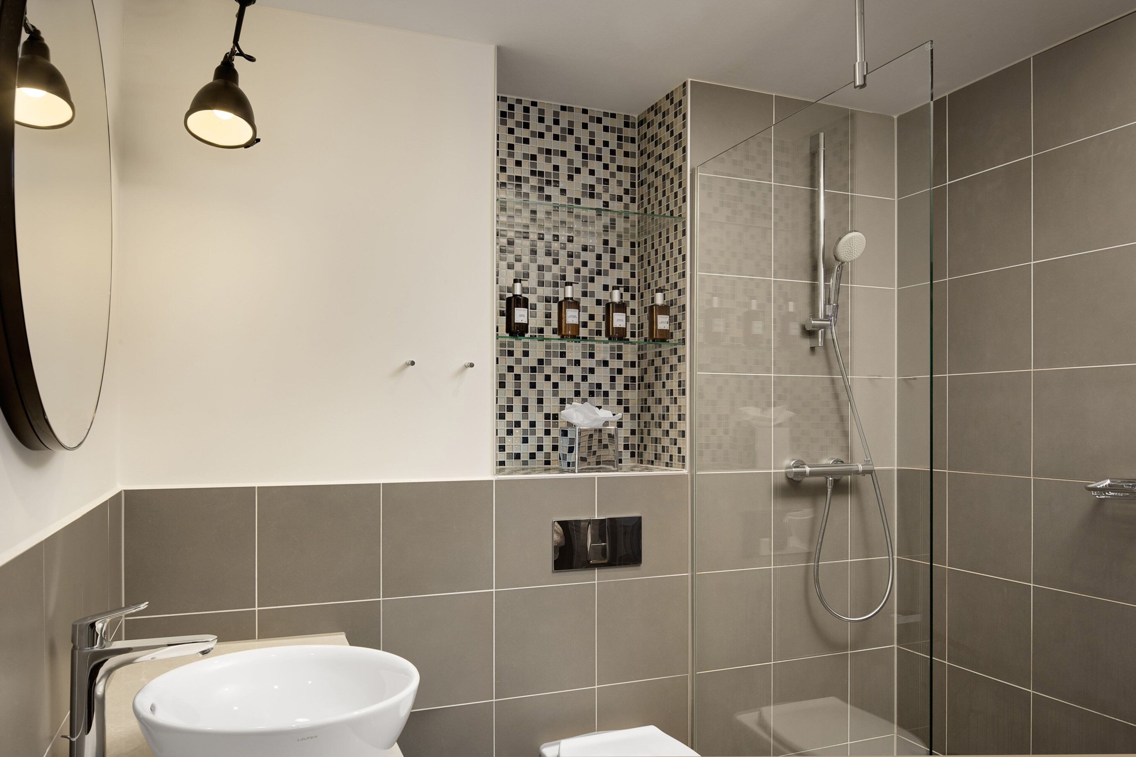 A modern bathroom with a white sink, a glass shower enclosure, and a tiled wall with a mosaic pattern.