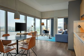 A modern hotel room with a dining area, a sofa, and a kitchen area.