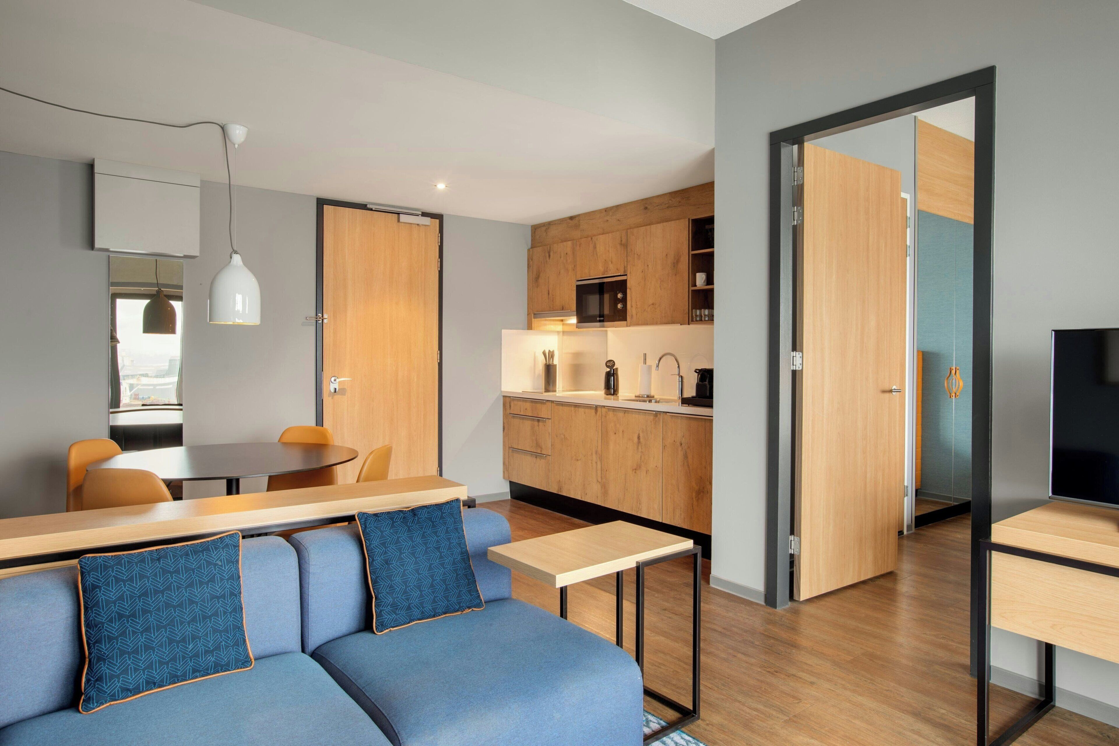 A modern apartment with a dining area, a kitchenette, and a living room with a sofa and a TV.