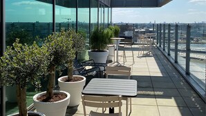 Una terraza en la azotea con plantas en macetas, mobiliario exterior y vistas del horizonte de la ciudad.