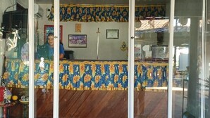 A reception area with a sign reading "RECEPCAO," a counter with a patterned curtain, and a brick floor. - Pousada Murici (Barreirinhas)