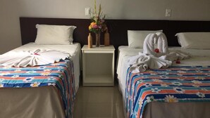 A hotel room with two beds, each with a floral bedspread and white pillows. There is a nightstand between the beds with a vase of flowers and two bottles. - Pousada Murici (Barreirinhas)