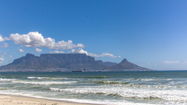 A beach with waves, a mountain, and a clear sky. - Mont Blu Condo (Cape Town)