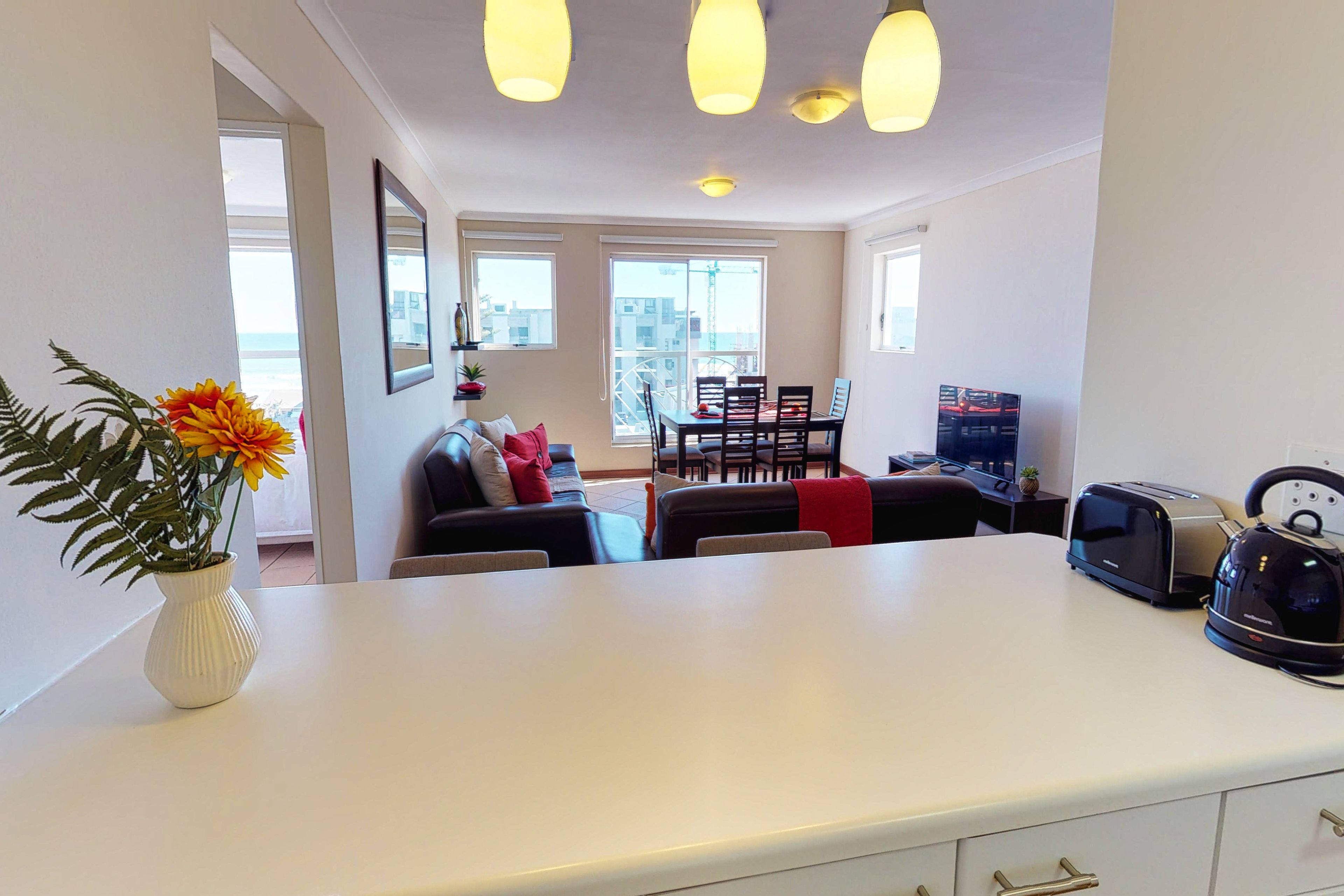 A modern living room with a white sofa, a dining table, and a kitchen area with a toaster and kettle.